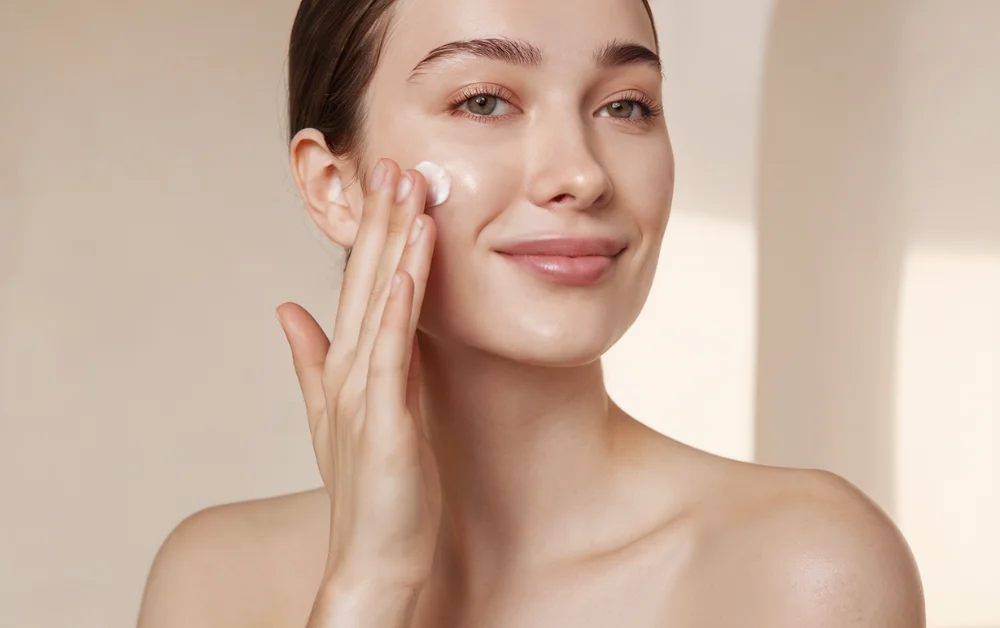 Smiling woman applying cream to her face, showcasing a simple skincare routine.